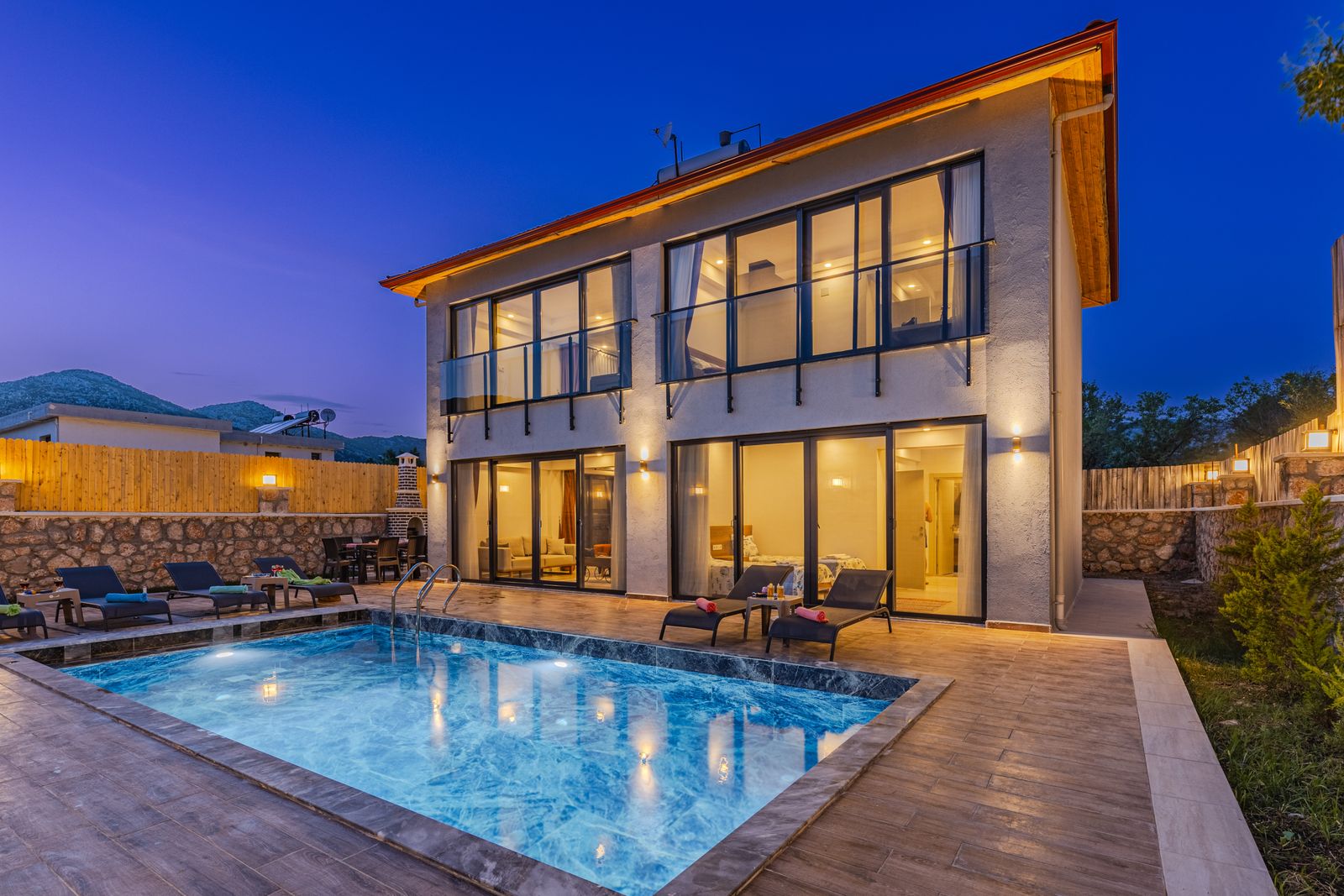 A finished backyard pool lit up at dusk beside a modern home