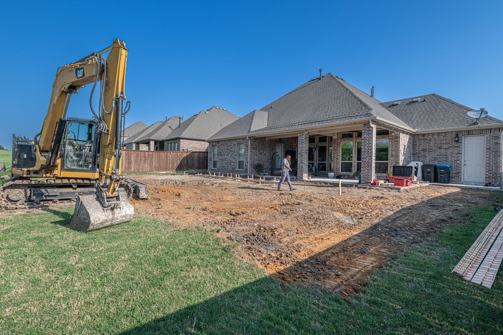 Excavator breaking ground in a staked-out backyard on the first day of construction