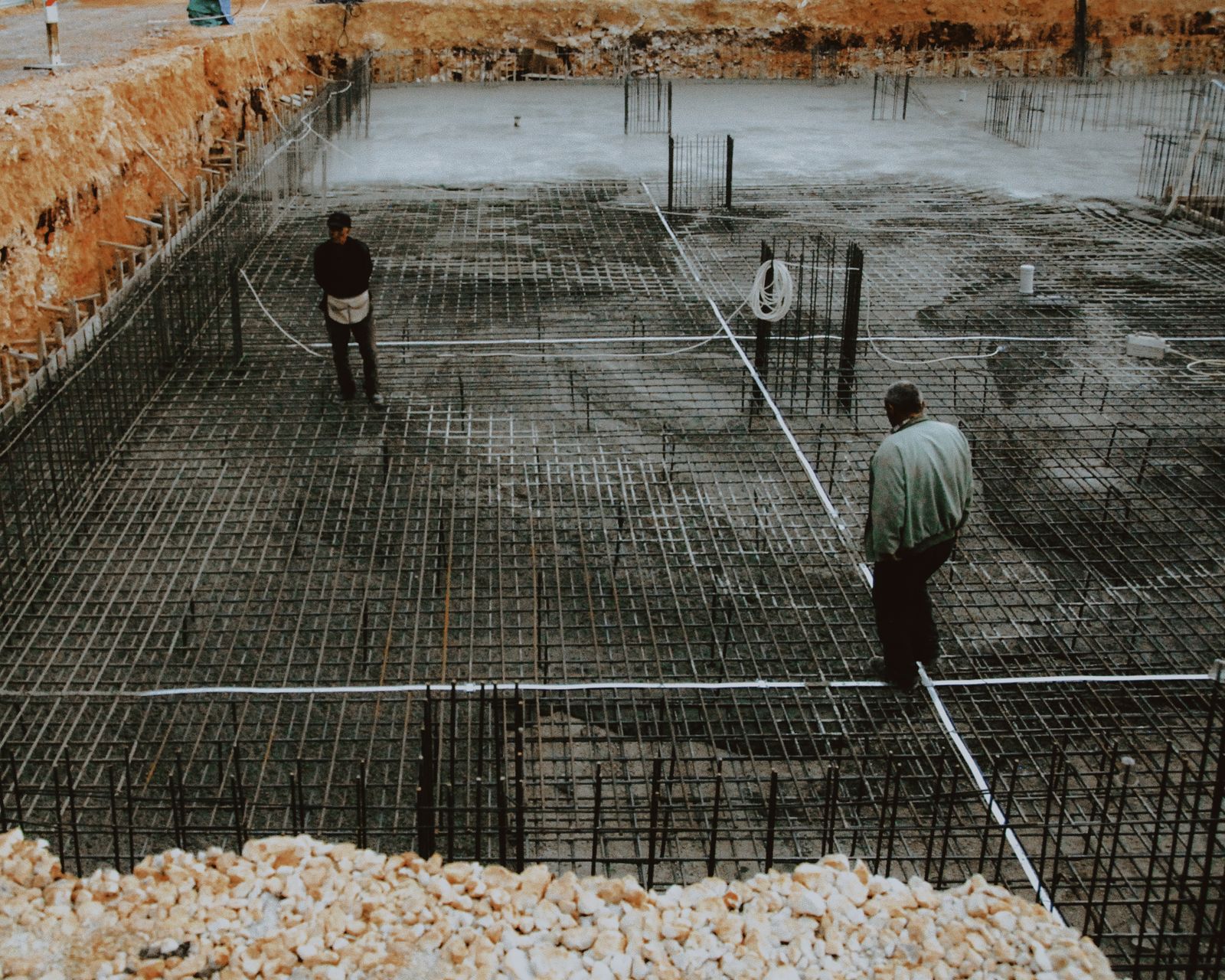 Two workers inspecting the rebar grid of a freshly excavated pool shell
