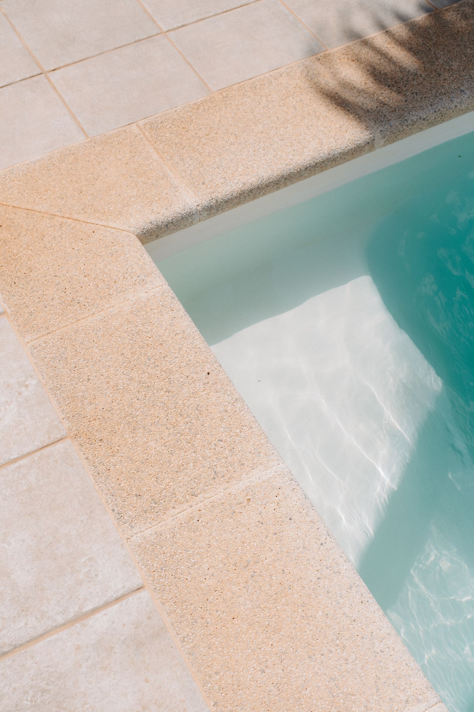 Stone coping and turquoise water at the corner of a newly finished pool